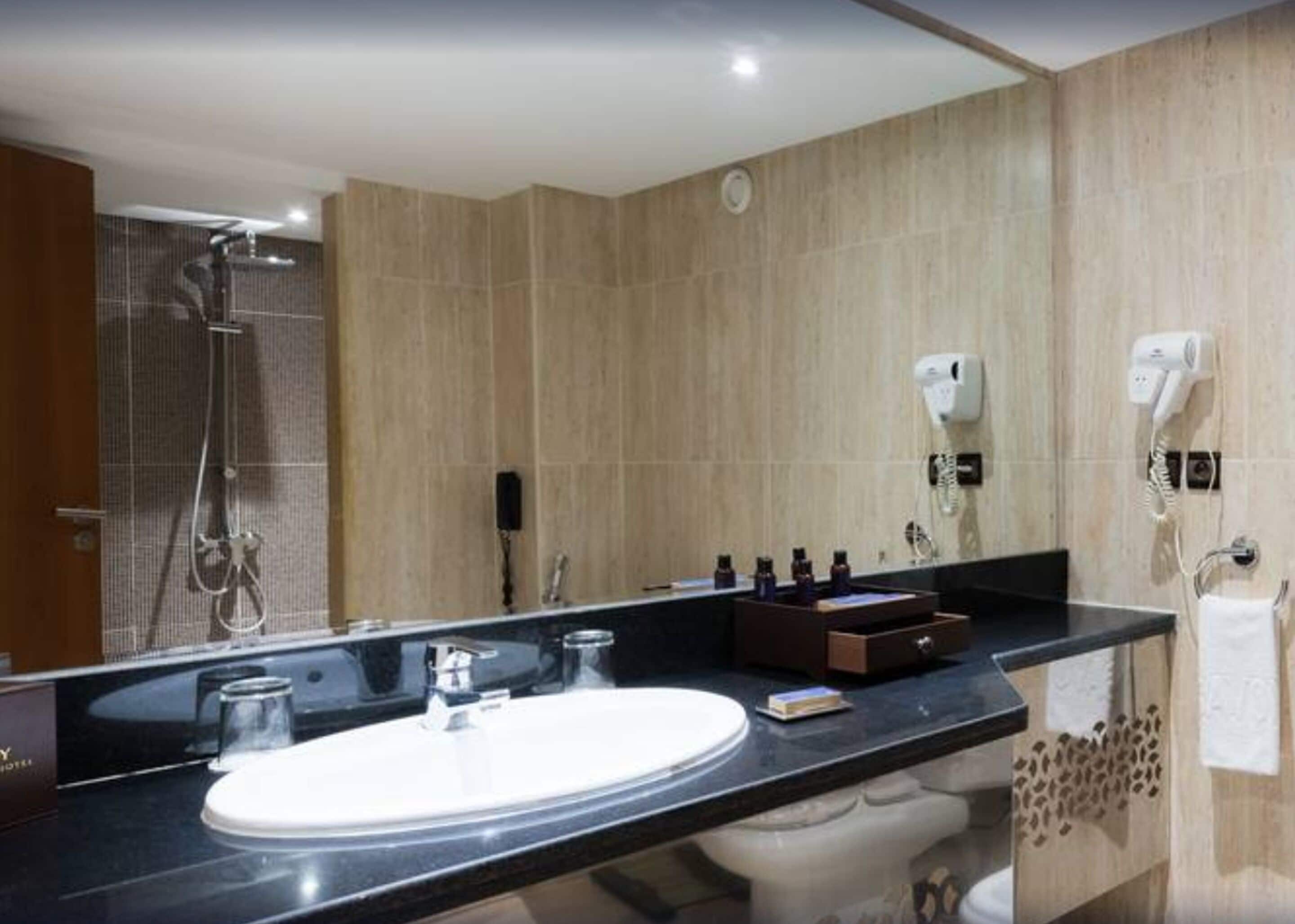 Une salle de bain moderne avec un grand miroir, un lavabo, une douche et deux sèche-cheveux fixés au mur.