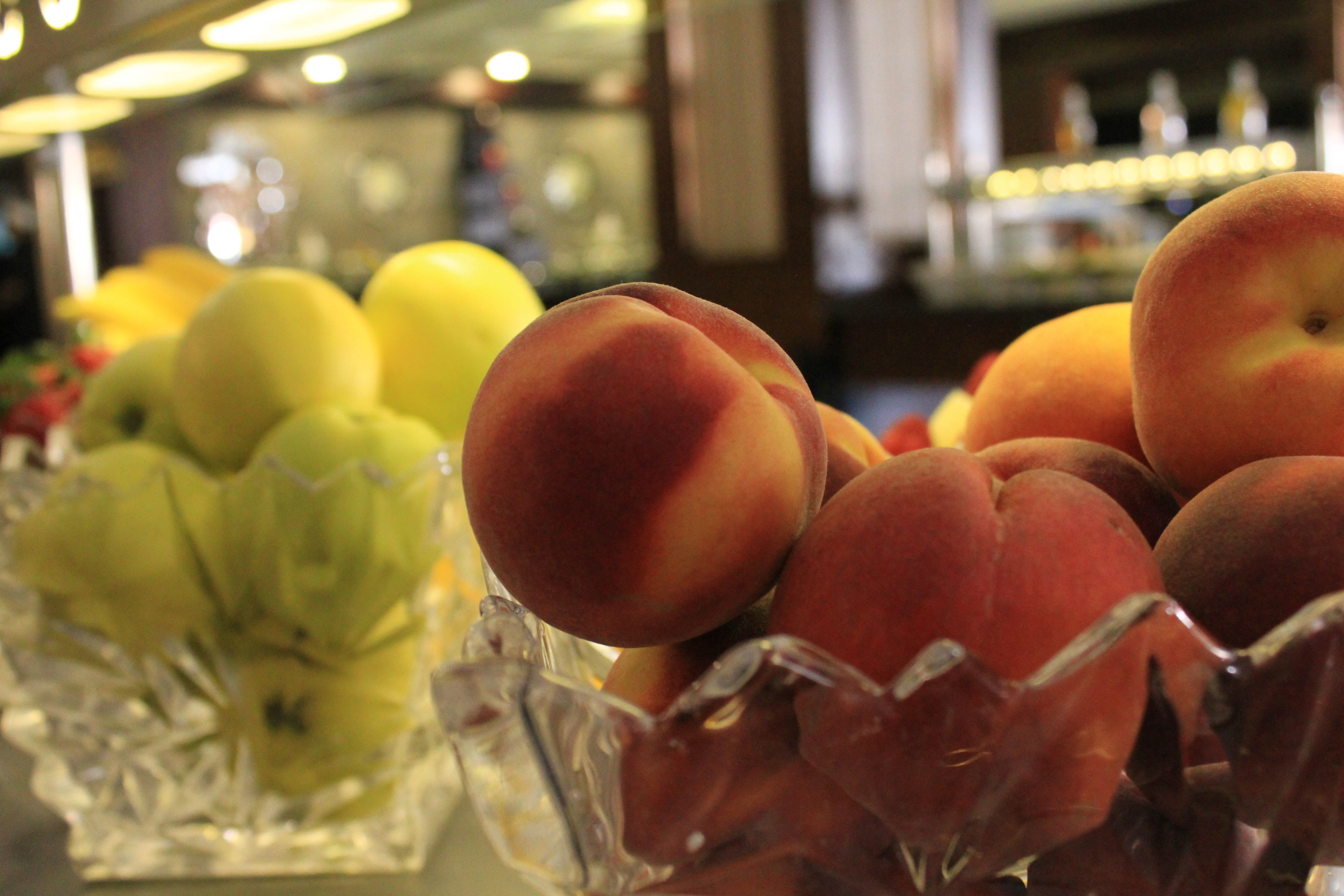 A fruit display with peaches and apples in a glass container.