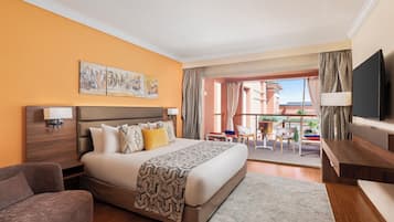 Habitación de hotel con una cama grande, un sofá, un televisor y un balcón con vistas a edificios.