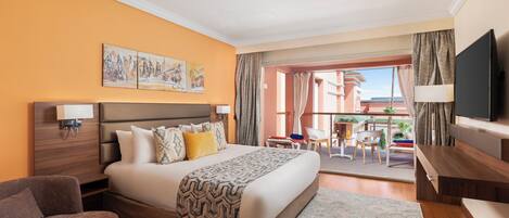 Une chambre d’hôtel avec un grand lit, un canapé, une télévision et un balcon donnant sur des immeubles.