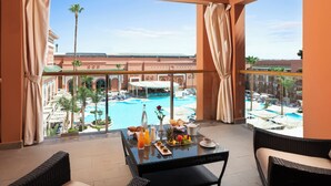 Un balcón con una mesa dispuesta para el desayuno, con vistas a una piscina y edificios del complejo.