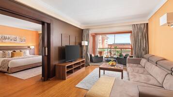 A hotel room with a bed, a TV, a sofa, a coffee table, and a view of the outside.