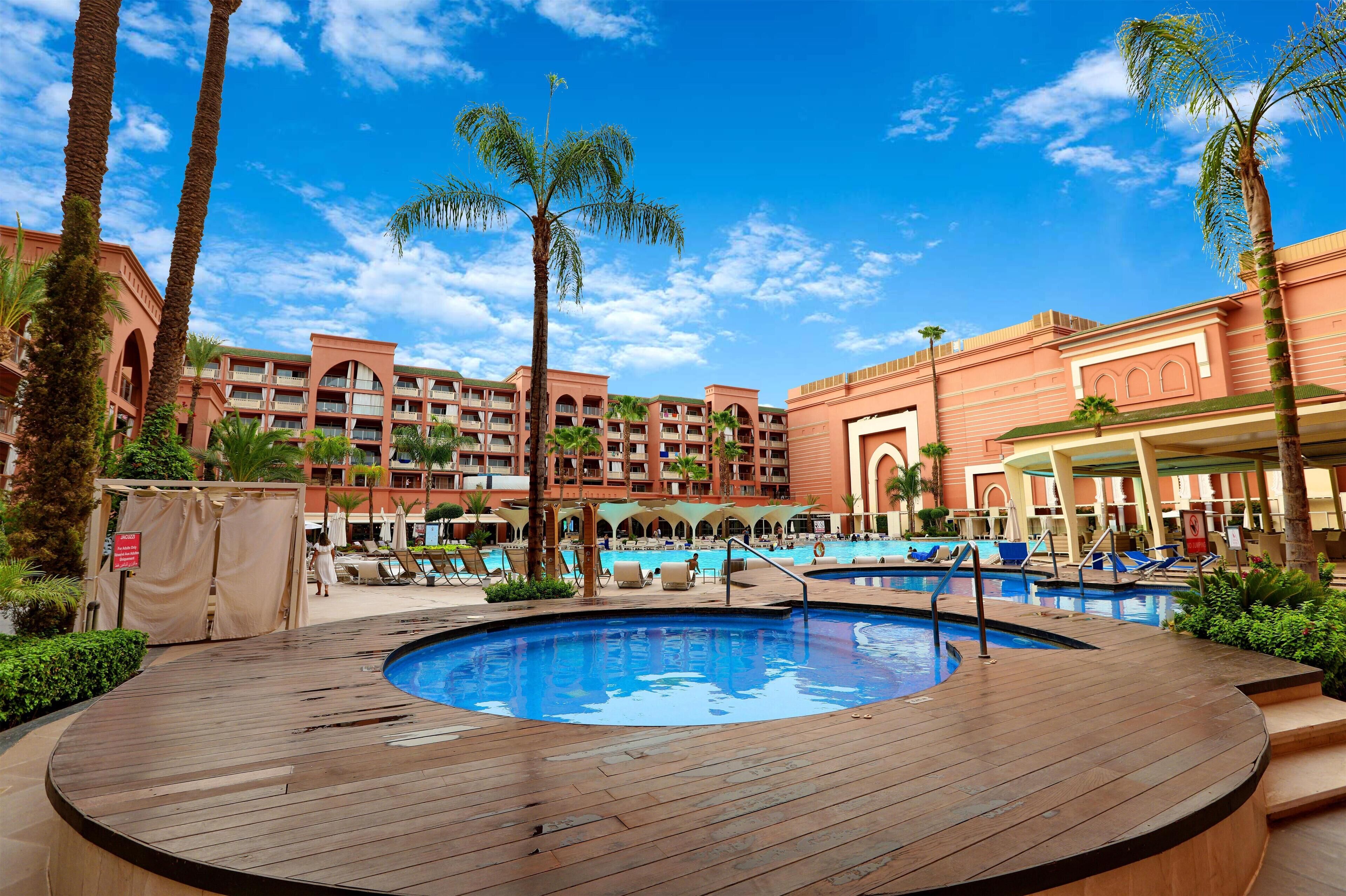Un hotel con una piscina grande, palmeras y un cielo azul despejado.