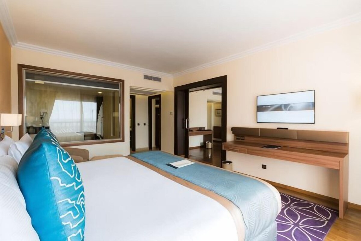 Una habitación de hotel con una cama grande, una mesita de noche, un televisor y un espejo.