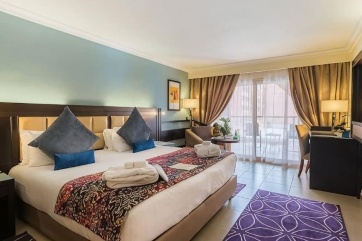 A hotel room with a large bed, a desk, and a view of the outdoors.