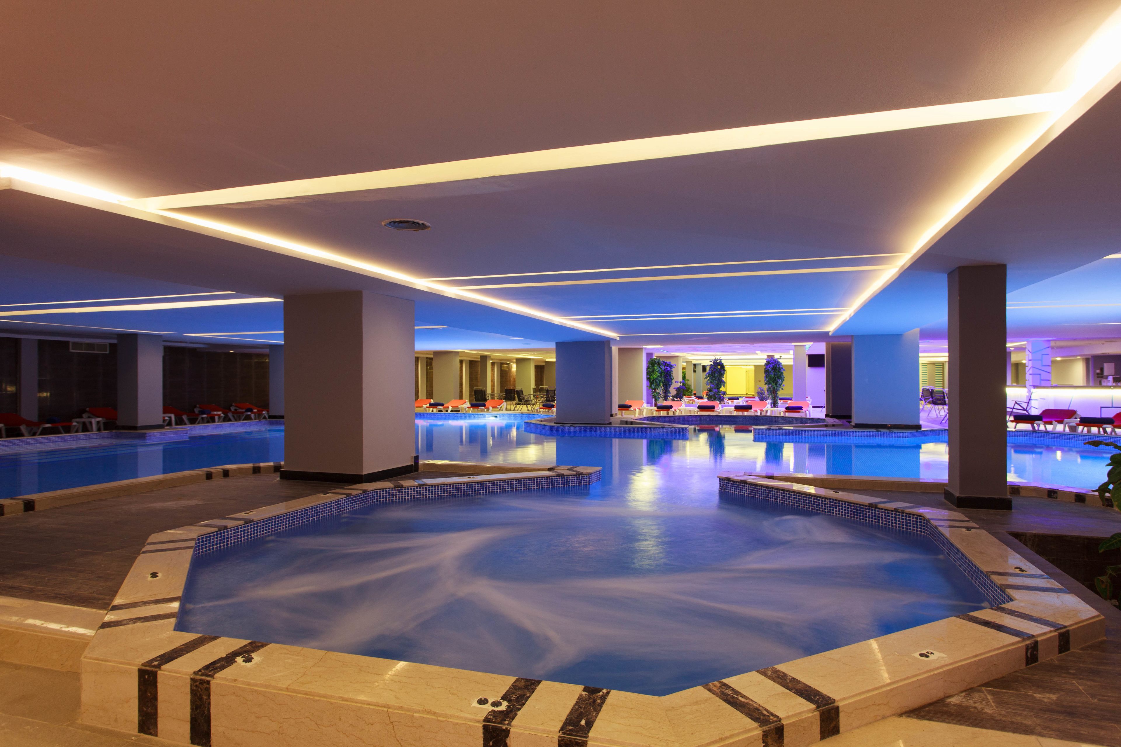 Una gran piscina cubierta con múltiples carriles, rodeada de zonas de estar y un bar.