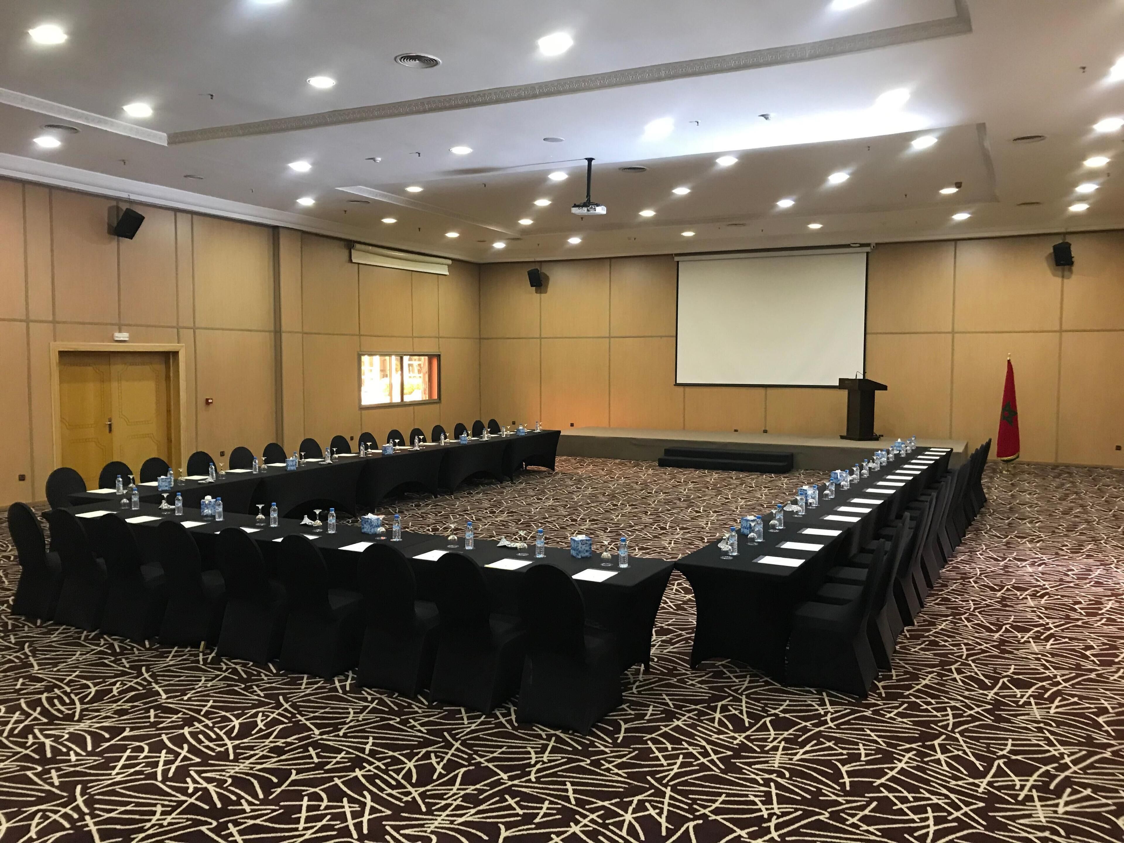 A conference room with a long table, chairs, a projector screen, and a podium.