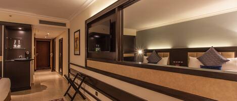 A hotel room with a large mirror, a bed, a desk, and a bathroom visible through an open door.