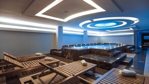 Un área de spa moderna con piscina climatizada, tumbonas de madera y un diseño de techo singular.