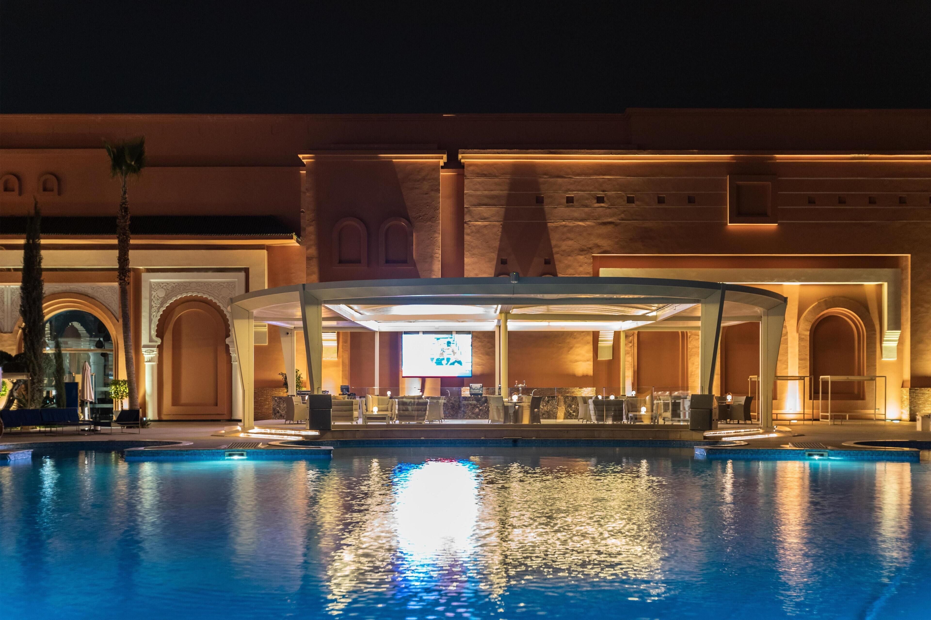 A pool area with a covered seating area, a large screen, and a bar.