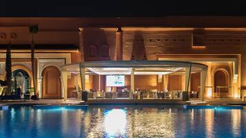 A pool area with a covered seating area, a large screen, and a bar.