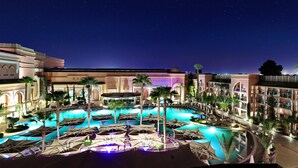 Zona de piscina hotelera con varias piscinas, palmeras y cielo nocturno.