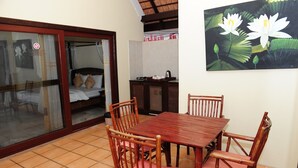 A room with a wooden dining table and chairs, a bed with white bedding, a sliding glass door, and a painting of lotus flowers on the wall. - Napalai Pool Villa Resort (Pattaya)