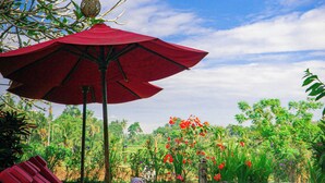 A red umbrella, a wicker lounge chair, and a garden with a water feature. - Uma Stana Villa (Ubud)