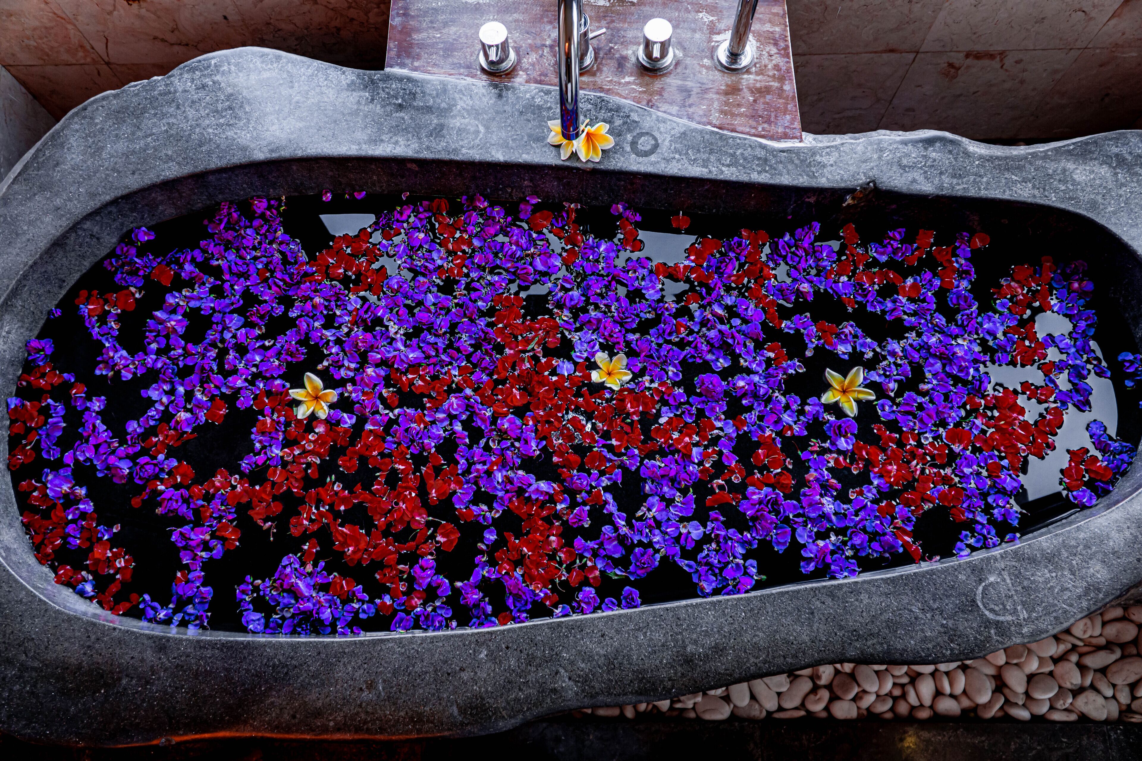 A stone bathtub filled with water and floating flowers.