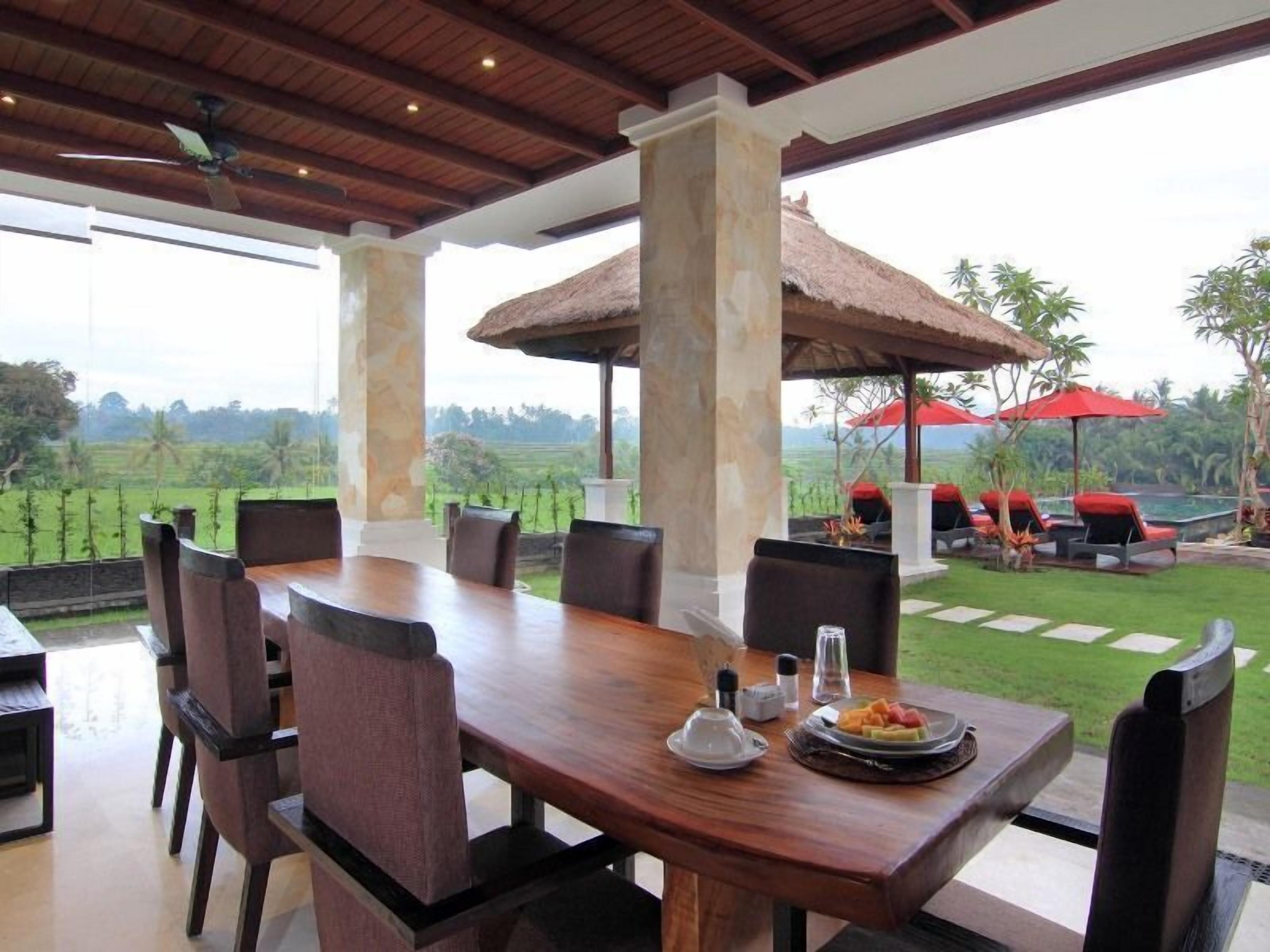 An outdoor dining area with a wooden table and chairs, a thatched umbrella, and a view of the surrounding landscape.