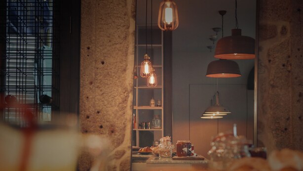 Un espace de restauration chaleureux, doté d’une décoration rustique, avec notamment des murs en briques apparentes, des luminaires suspendus et un assortiment de pains et de viennoiseries présentés sur le comptoir.