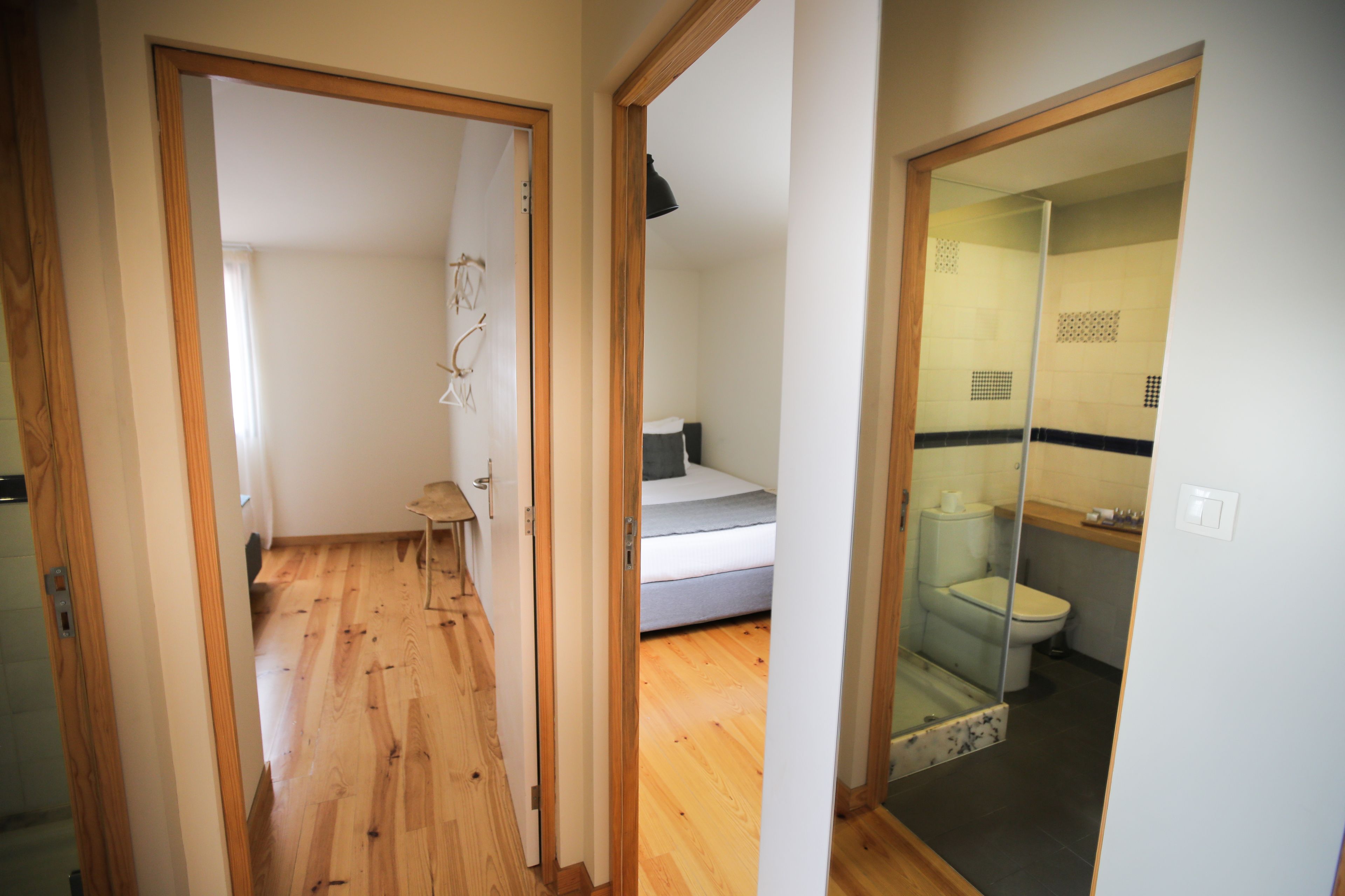 Ein schmaler Flur führt zu einem Schlafzimmer mit Bett und Nachttisch, sowie zu einem Badezimmer mit Toilette und Duschkabine.