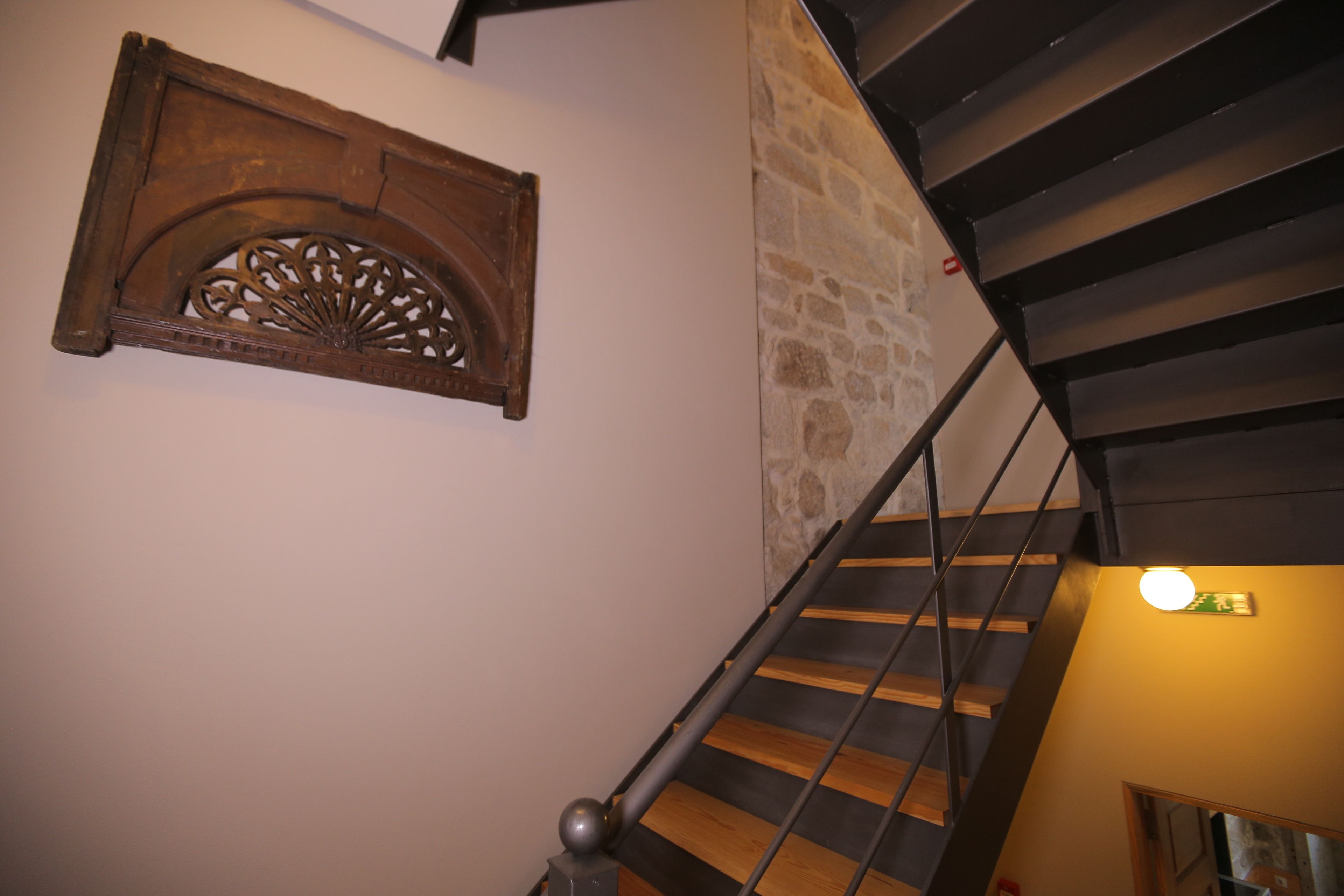 A staircase with wooden steps and metal railings, a stone wall, and a decorative wooden panel on the wall.