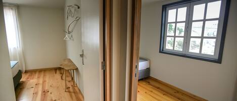 A room with wooden flooring, a window with blinds, and a door with a mirror.