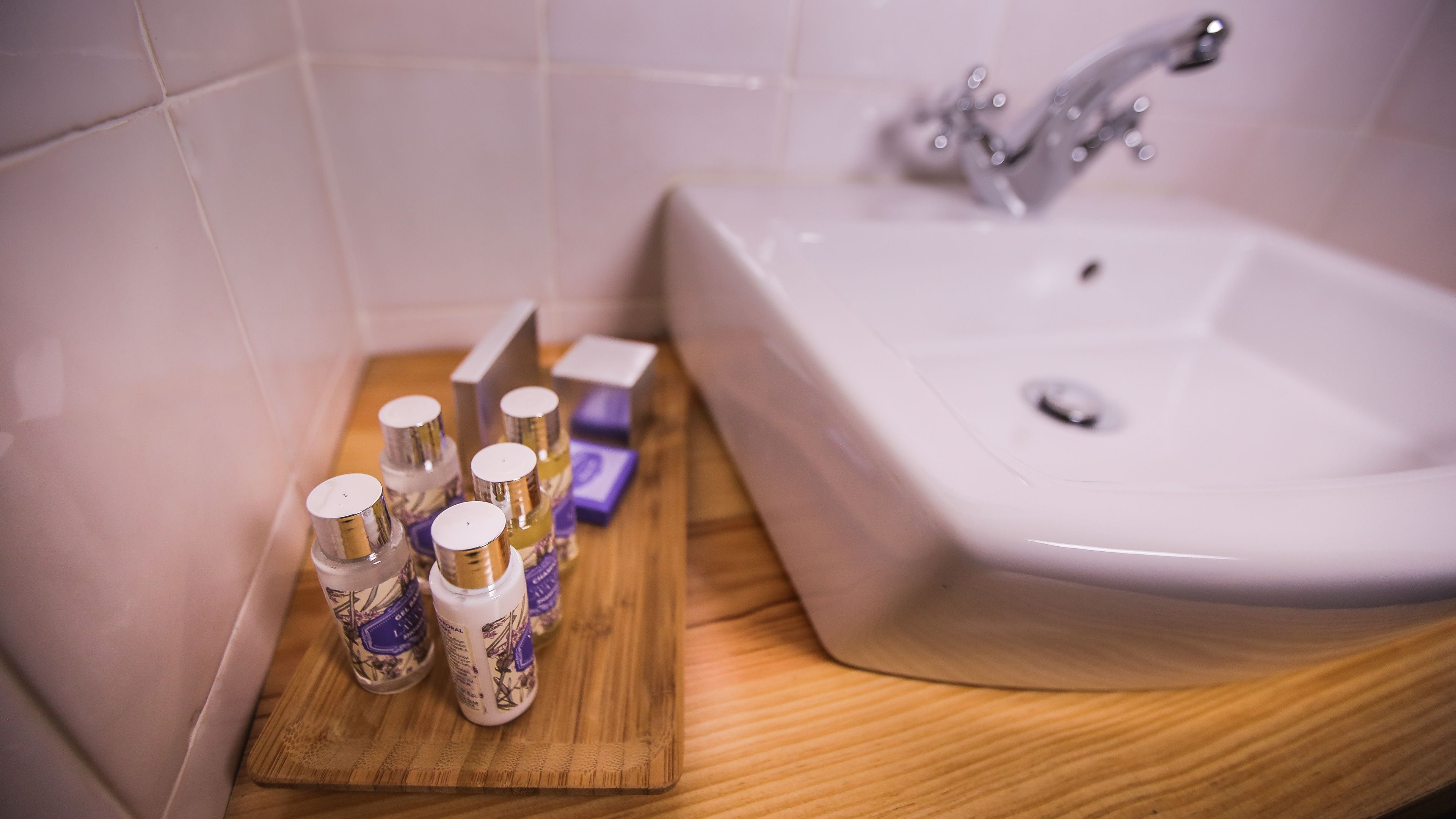 Ein Badezimmer mit einem weißen Waschbecken, einem hölzernen Waschtisch und verschiedenen Toilettenartikeln.