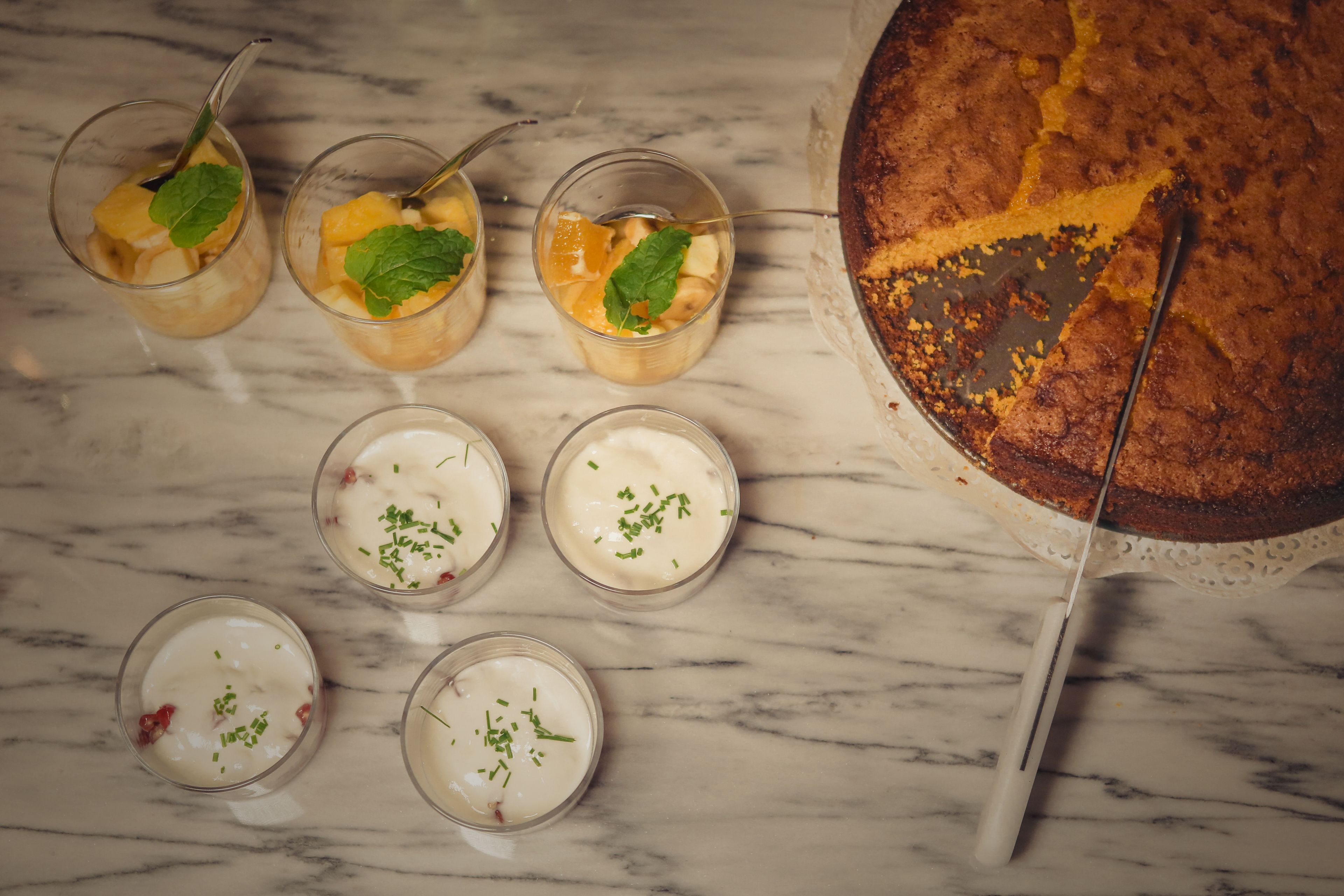 A marble table with five glasses of dessert, each garnished with mint leaves, and a partially sliced cake on a cake stand.