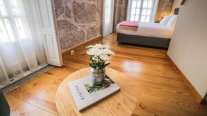 Une pièce avec un plancher en bois, un mur en pierre, un lit recouvert d’une courtepointe blanche et un vase rempli de fleurs blanches posé sur une table.