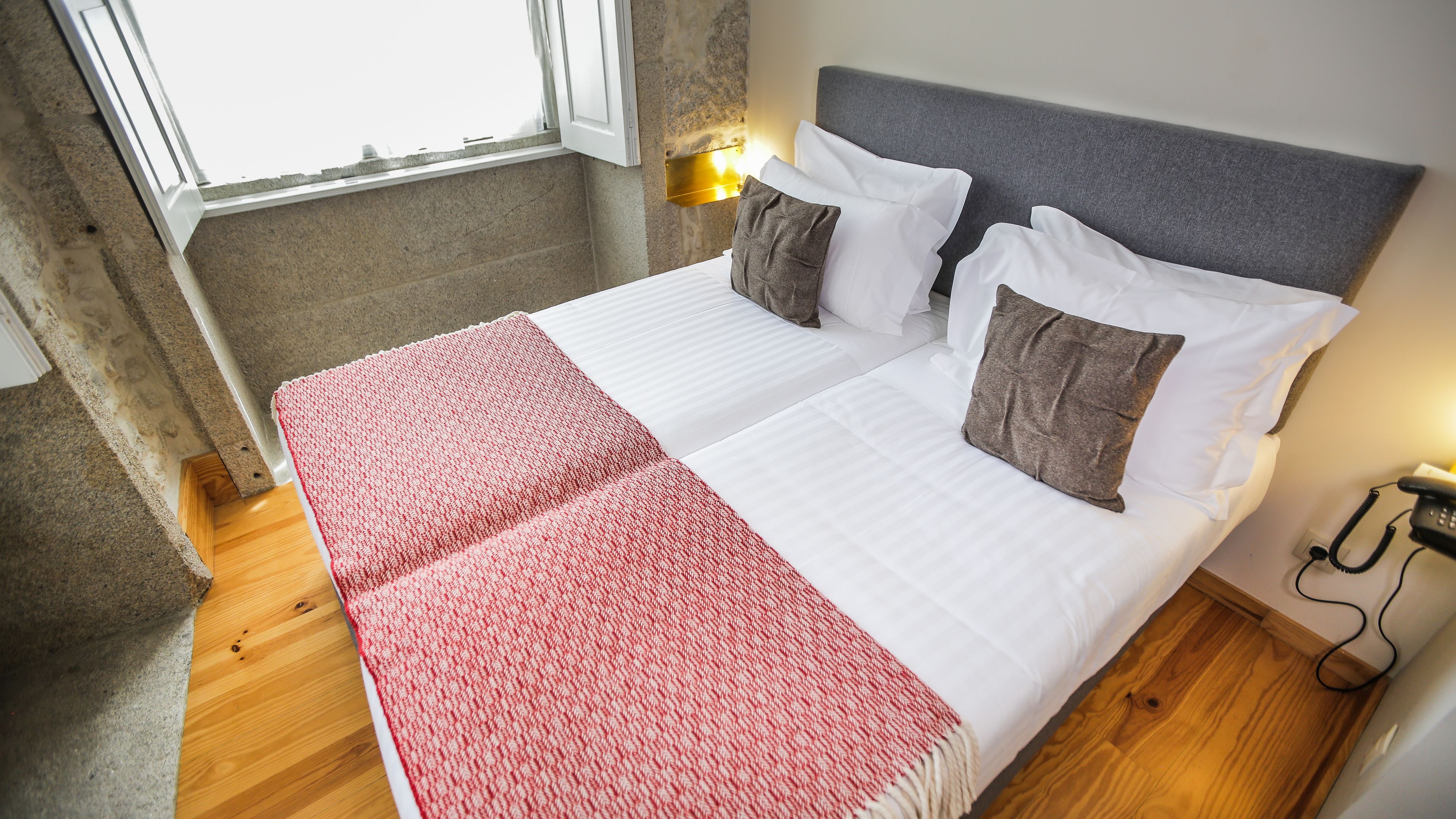 A neatly made bed with white and brown pillows, a red and white blanket, and a wooden floor.