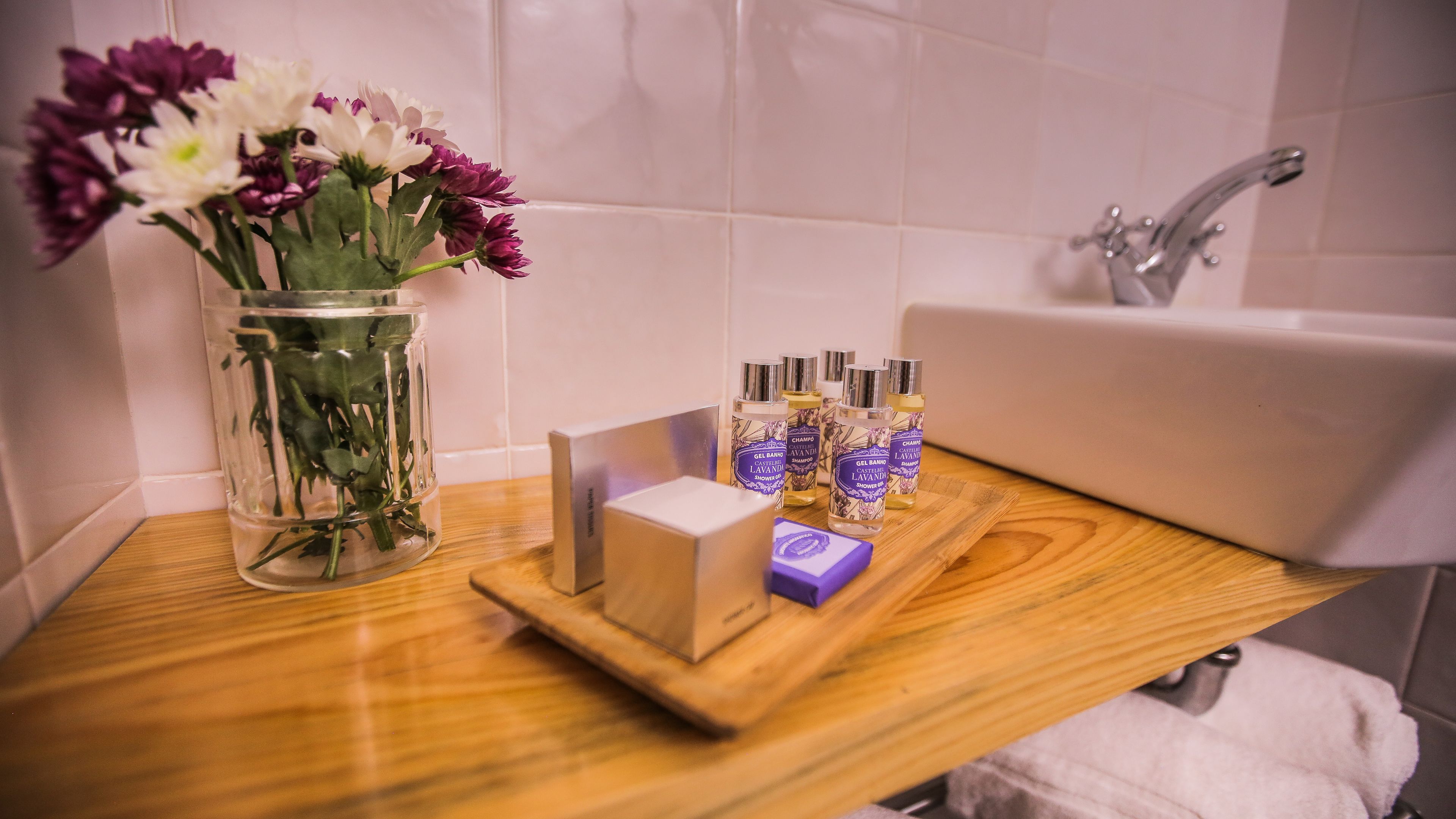 Ein Badezimmer-Waschtisch mit Holzplatte, eine Glasvase mit Blumen und eine Ablage mit Toilettenartikeln.