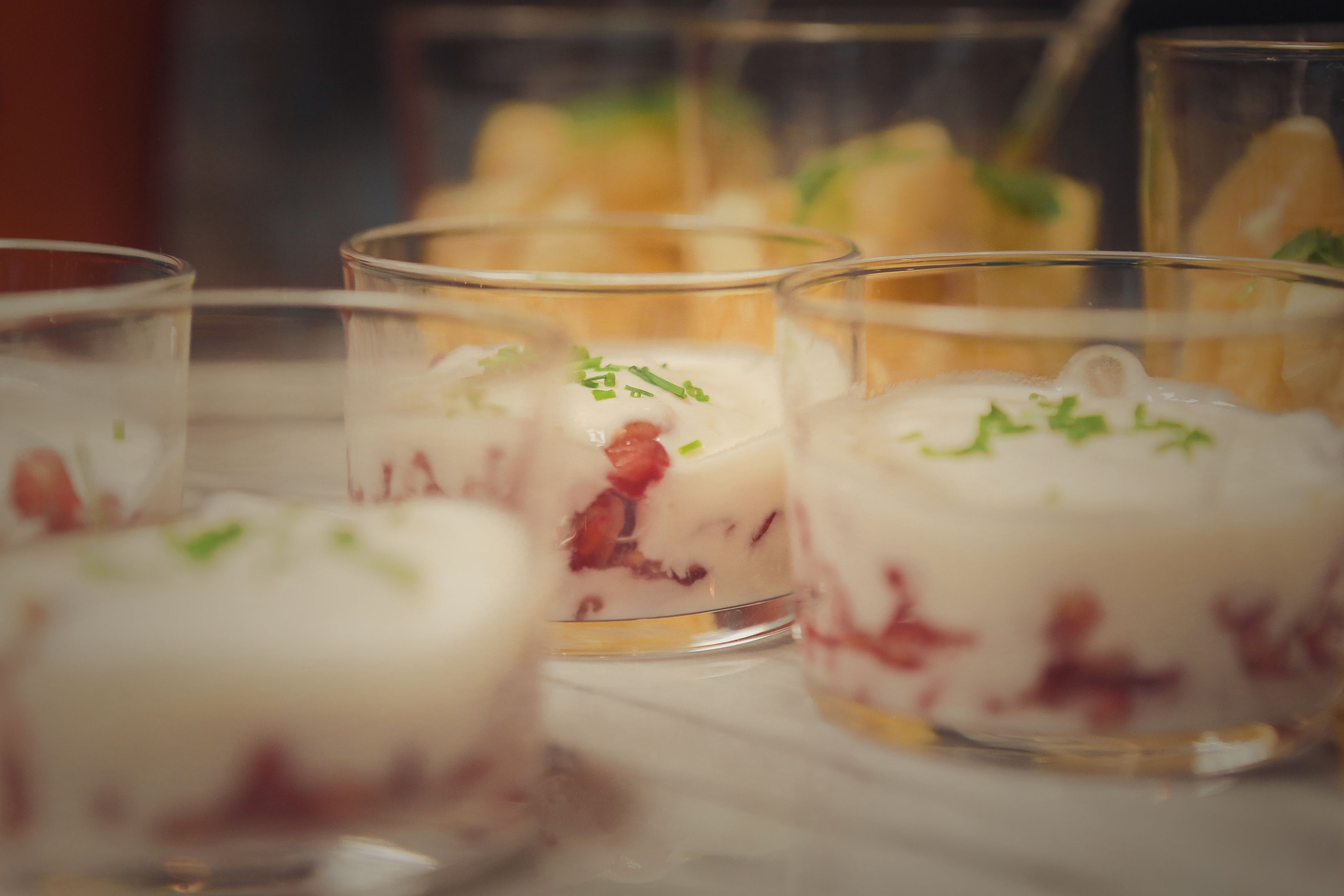 Ein Dessert mit Schichten aus weißen und roten Bestandteilen, garniert mit grünen Kräutern, serviert in Gläsern.
