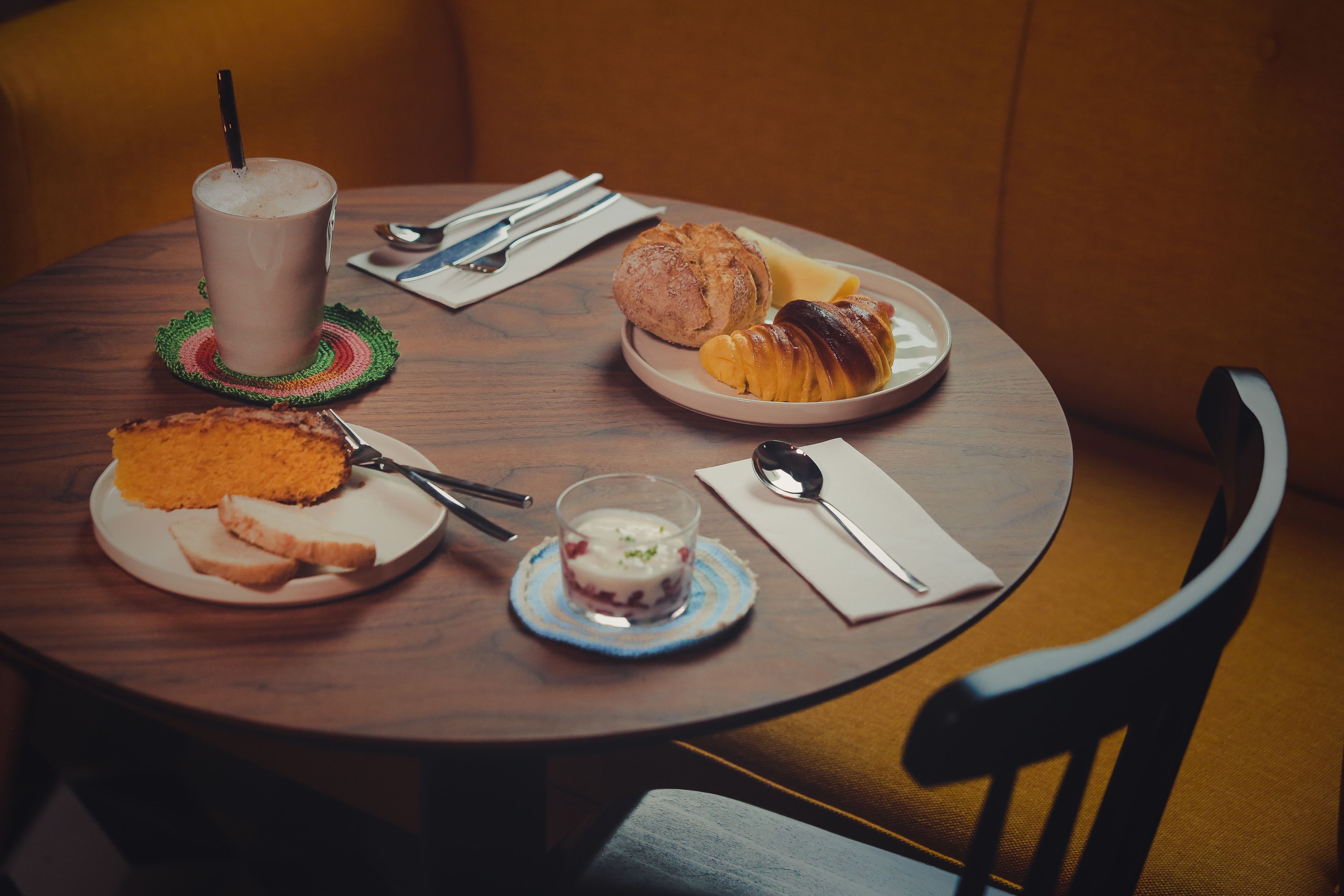 A round wooden table with a plate of croissants, a glass of milk, and a slice of cake.