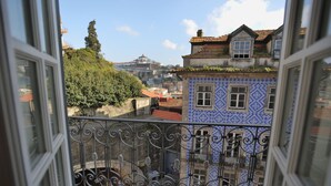 Une vue depuis un balcon orné de balustrades en fer forgé, donnant sur un immeuble dont la façade est recouverte de carreaux bleus et blancs et le toit de tuiles rouges.