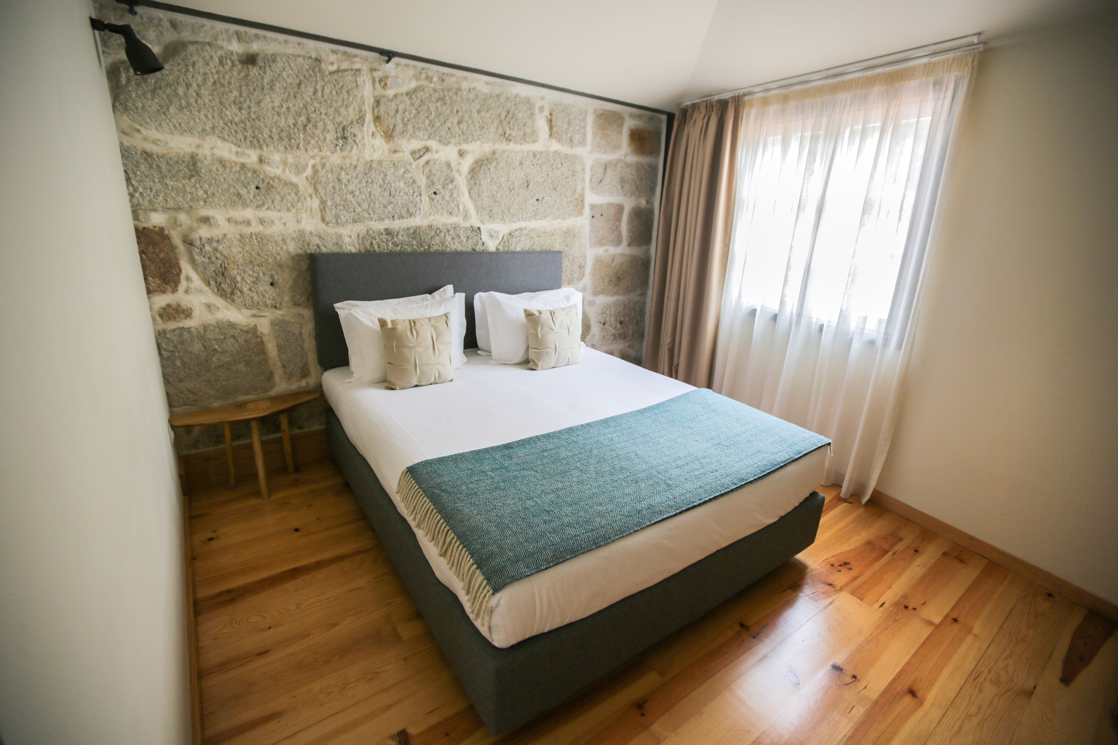 Une chambre avec un mur en pierre, un lit doté d’une tête de lit sombre et un plancher en bois.