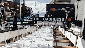 A long dining table set for a meal with a view of a snowy mountain in the background. - Super G (Courmayeur)