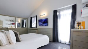 A modern hotel room with a large bed, a flat-screen TV, a mirror, a dresser, and a window with curtains. - Super G (Courmayeur)
