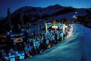 Pendiente nevada con una multitud reunida en un área decorada para un evento, que cuenta con un escenario y un cartel que dice "TONICX".