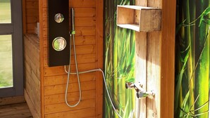 Una cabaña de madera con zona de ducha, una pared con motivos de bambú, un ventilador de techo y una ventana.