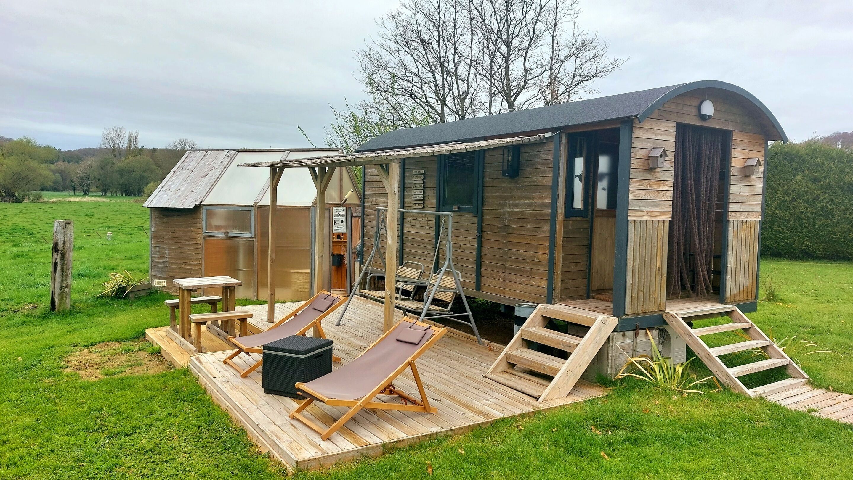 Een houten hutje met een terras, twee loungestoelen, een tafel en een kleine trap naar de ingang.