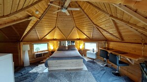 Un dormitorio acogedor en el ático, con techo inclinado, una cama, dos mesitas de noche, un escritorio y una silla.