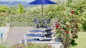 Een zwembadterras met ligbedden, een tafel en een parasol.