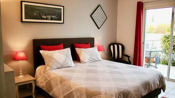 Een slaapkamer met een groot bed, twee nachtkastjes met lampen, een stoel, een lijst met afbeelding en een geometrisch wanddecoratie.
