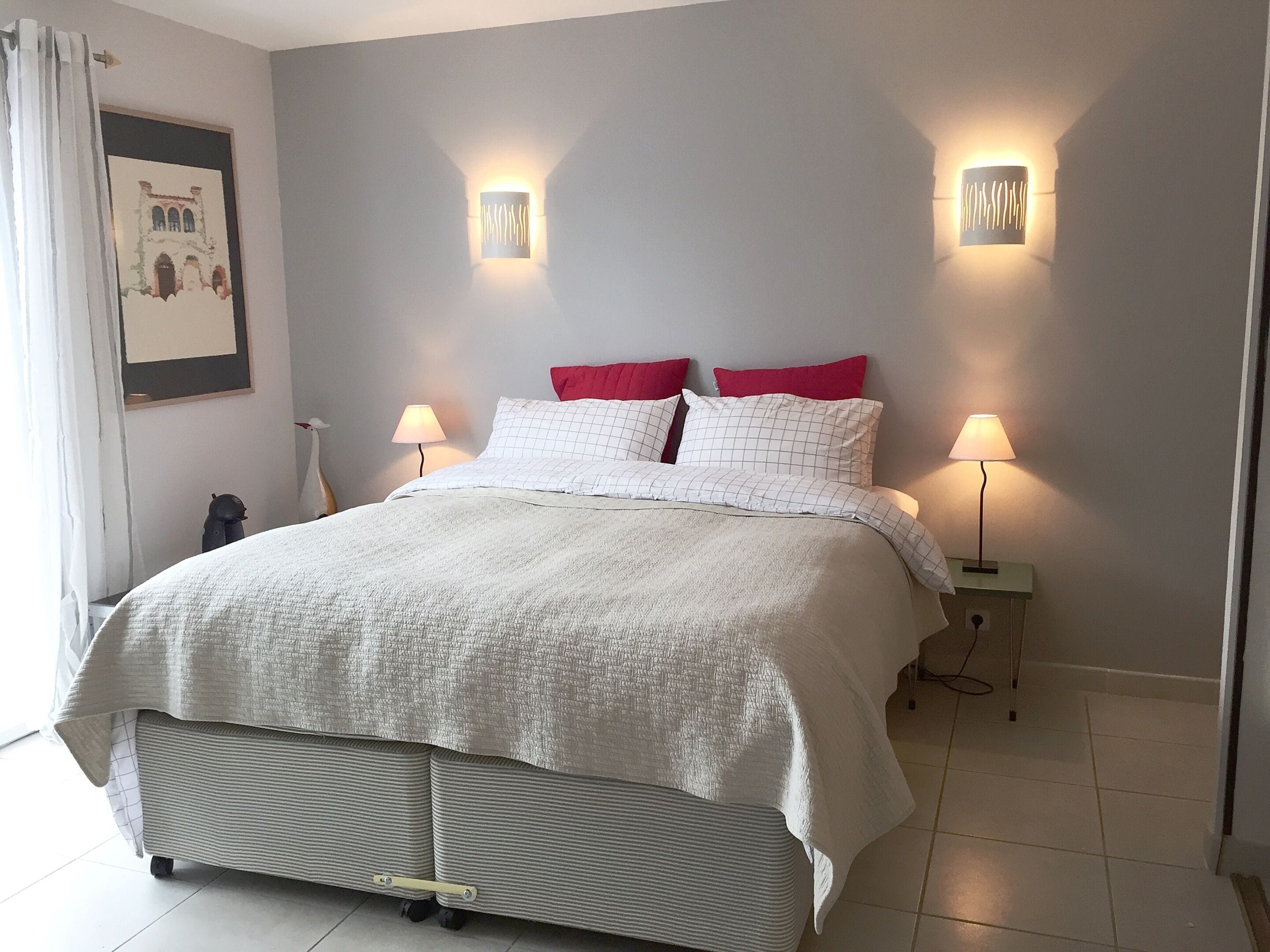 A bed with a white quilt, two red pillows, and two wall-mounted lamps.