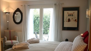 Een hotelkamer met een groot bed, een stoel, een lijst met een afbeelding en uitzicht door het raam.