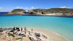 A beach with clear turquoise water, rocky outcrops, and people sunbathing. - Oriana Hotel (St. Paul's Bay)