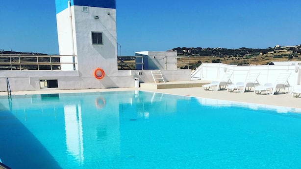 A clear blue pool with a lifebuoy, a white building, and a view of the landscape. - Oriana Hotel (St. Paul's Bay)