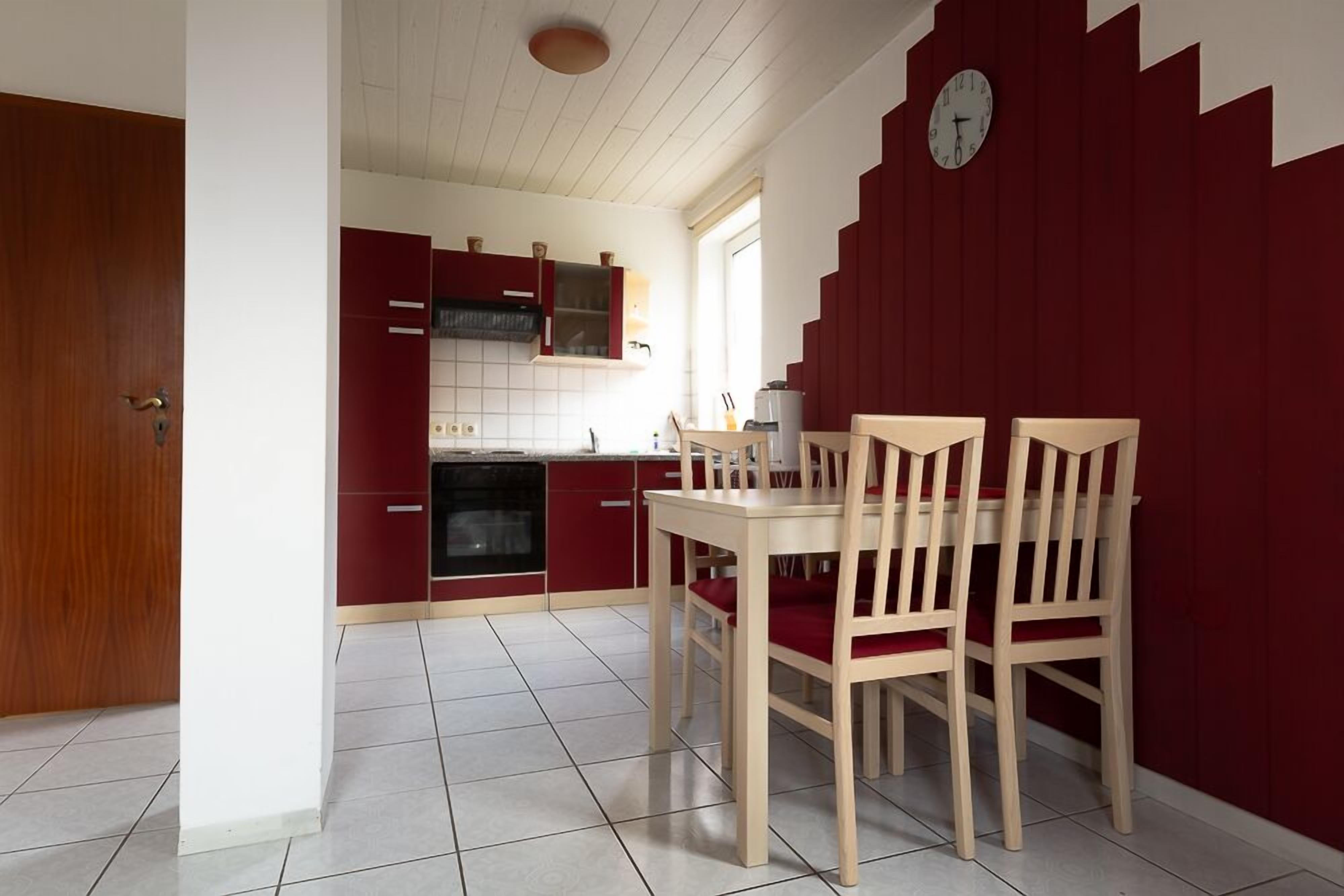 Een keuken met rode kastjes, een eettafel met vier stoelen en een klok aan de muur.