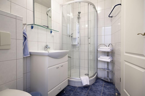 Un baño moderno con ducha de vidrio, lavamanos blanco y toallero.