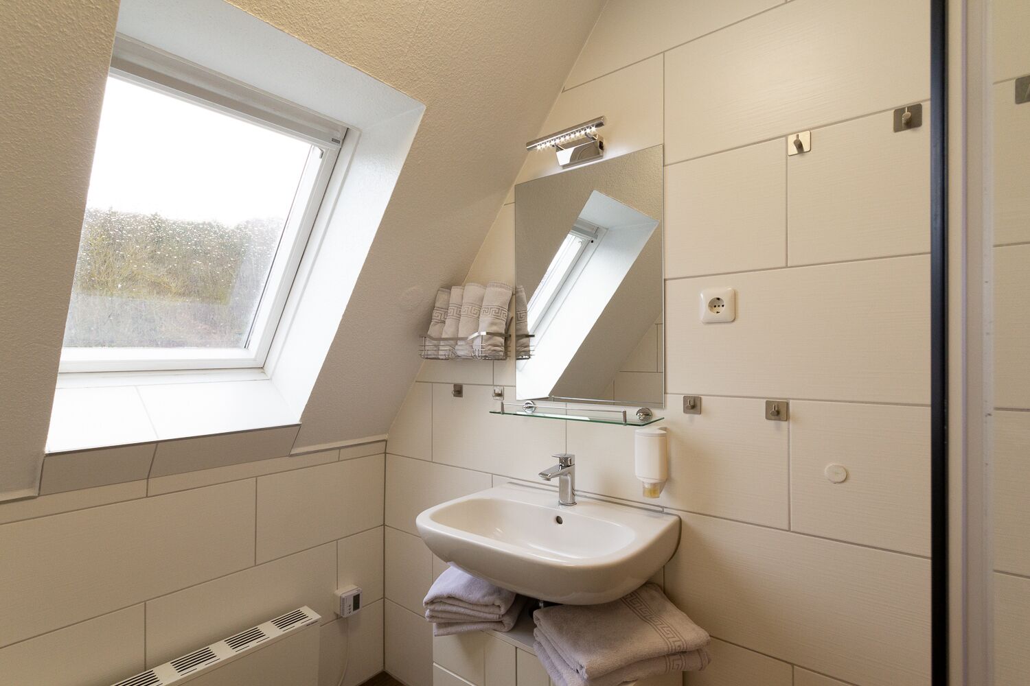 Een kleine, moderne badkamer met dakraam, een wastafel, spiegel en handdoekhouder.