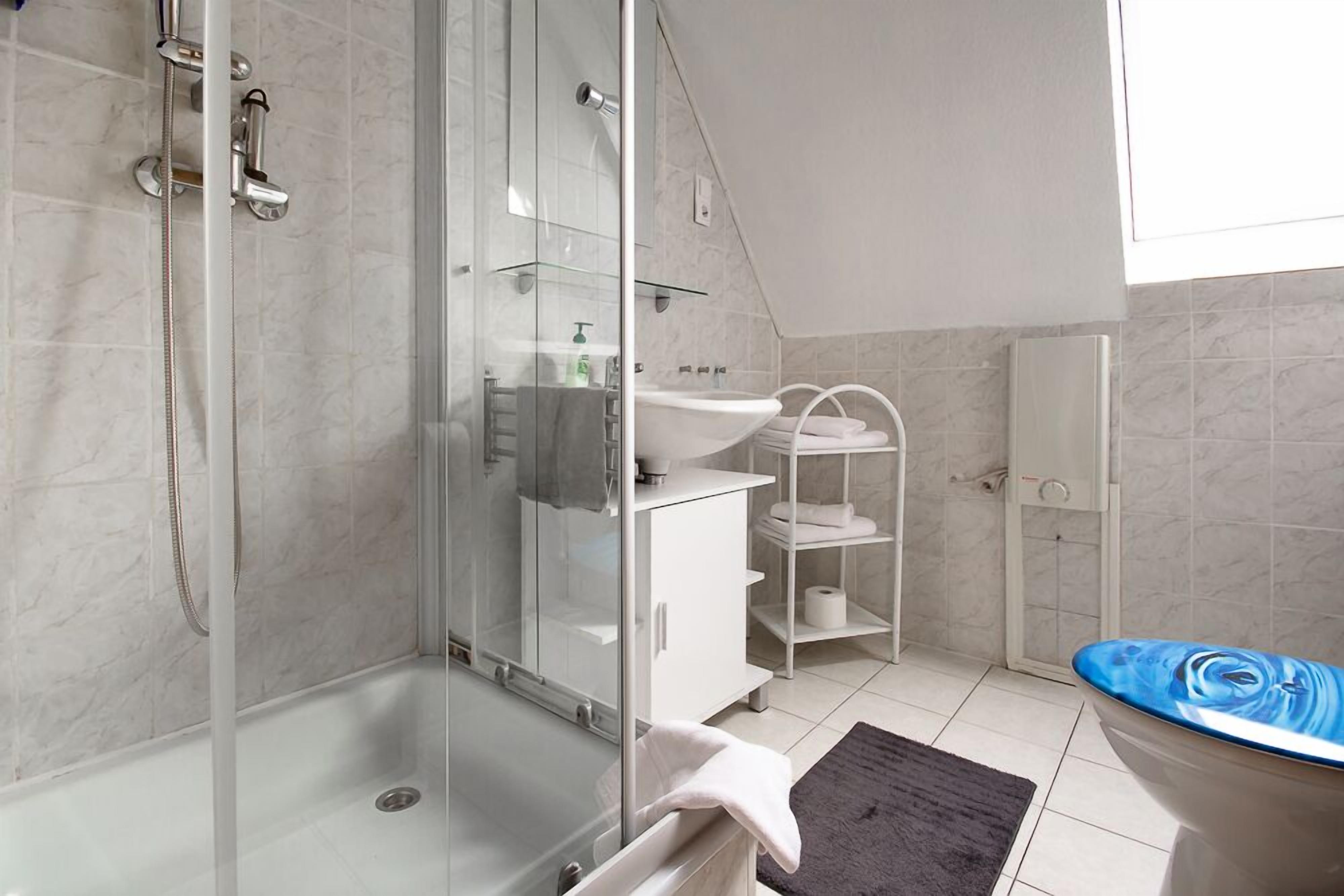A modern bathroom with a glass shower enclosure, a white sink, and a bathtub with a blue design.