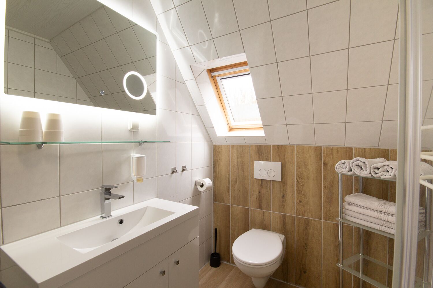 Een moderne badkamer met een wit wastafelmeubel, spiegel en toilet. Boven het wastafelmeubel bevindt zich een glazen plank en er is een handdoekrek met handdoeken.